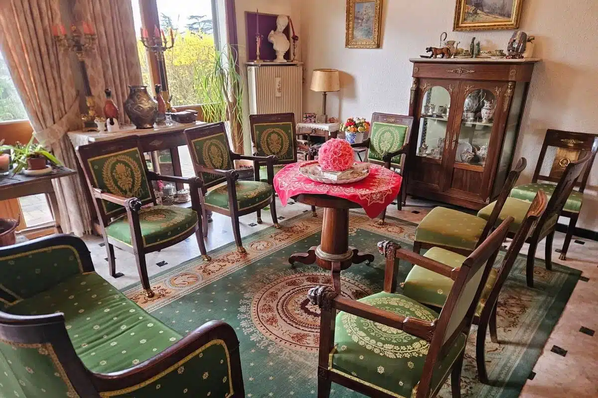 Salon meublé avec fauteuils anciens, vitrine, tableaux et objets d'art illustrant les antiquités achetées par Antiquités Maillot à Grenoble.